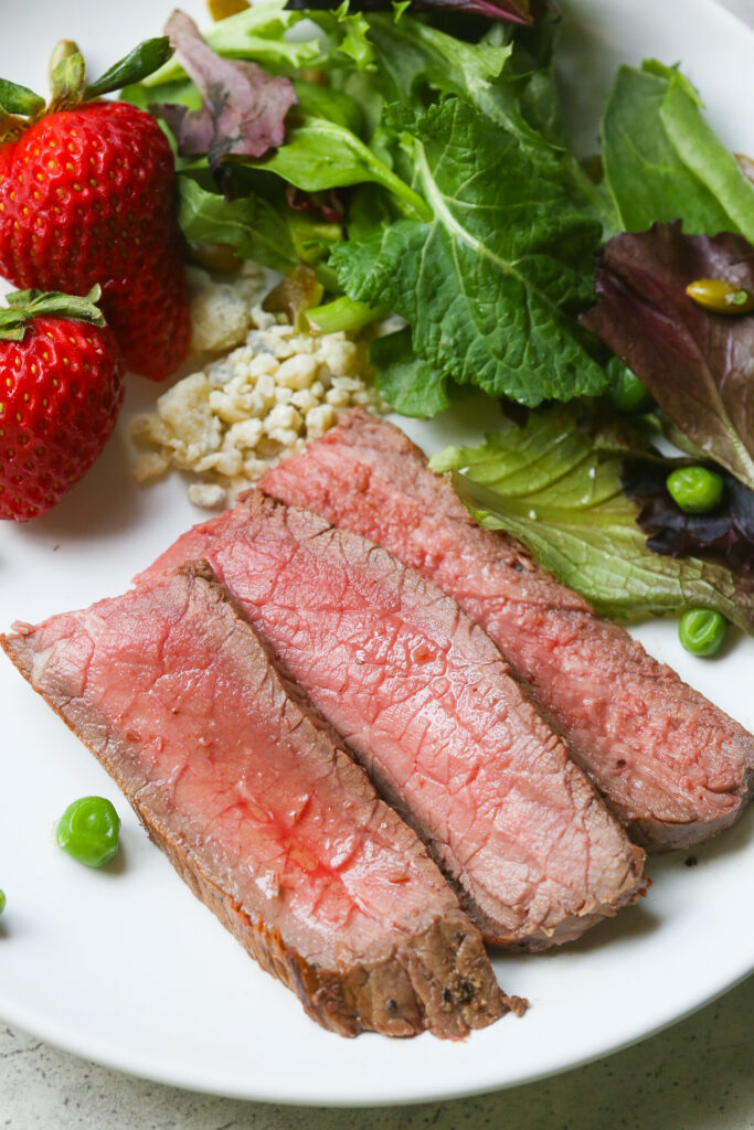 Close up pics of easy London Broil on white place with salad in the background