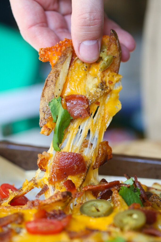 Close up of cheese pull of fingers pulling cheese fries with bacon and cilantro
