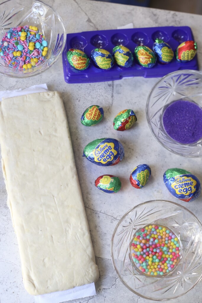 Ingredients for easy Cadbury cream egg chocolate croissants with puff pastry which includes puff pastry, Cadbury creme eggs, and colored sugar