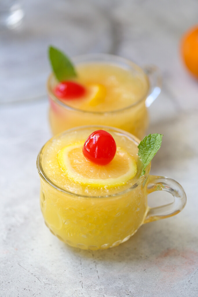 slushy pineapple non-alcoholic party punch in small punch glass with lemon slice, mint leaf, and cherry on top