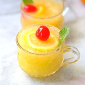 slushy pineapple party punch in small punch glass with lemon slice, mint leaf, and cherry on top