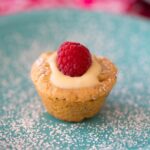 lemon thumbprint cookie filled with creamy lemon curd and a raspberry on a blue plate dusted with powdered sugar