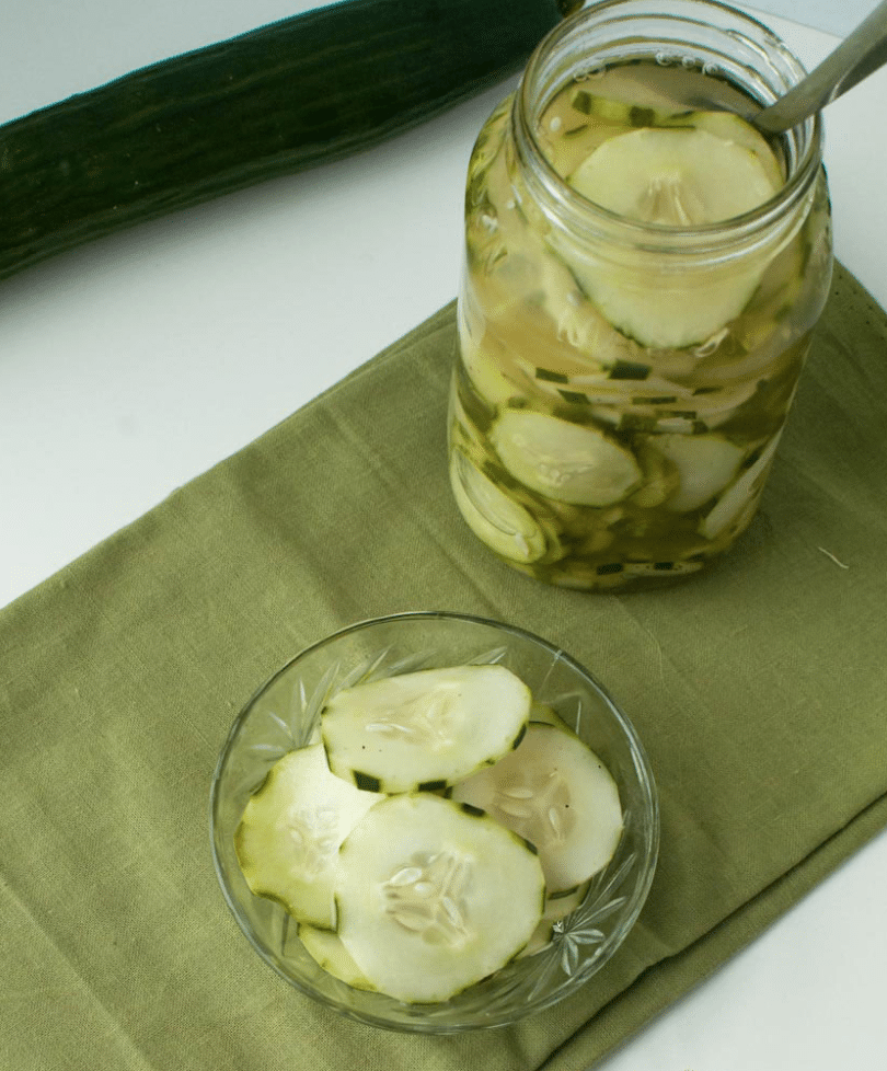 cucumbers and vinegar in a bowl and in a mason jar on a table with a green cloth napkin
