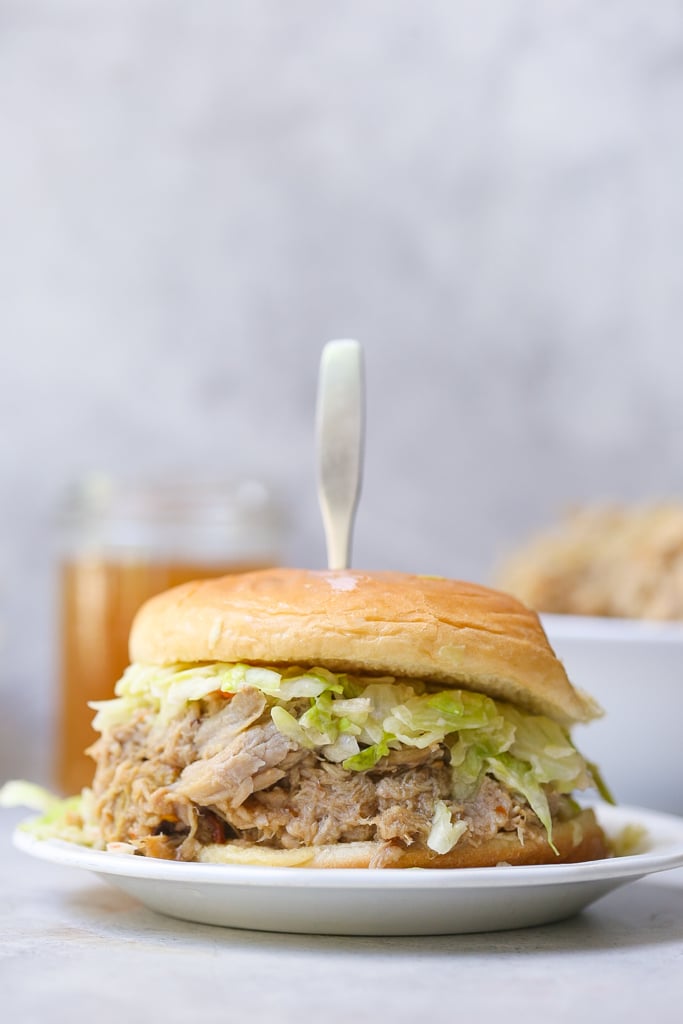 Carolina pulled pork sandwich on white plate with silver sandwich holder and green slaw