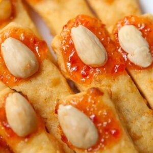 witch fingers cheese straws with red pepper jelly and marcona almonds on a white plate