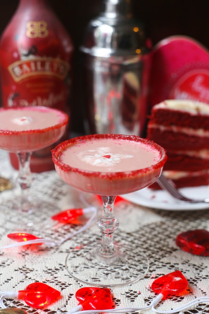 Baileys red velvet martinis in glasses with red sugared rim with a slice of red velvet cake in the background