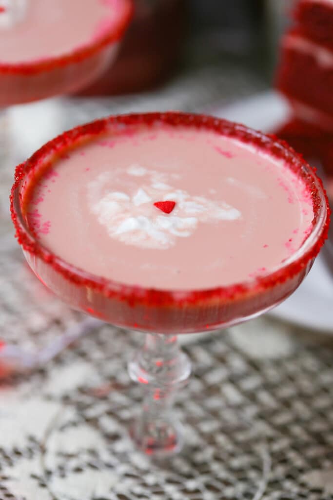 Red velvet chocolate martini in a martini glass rimmed with red sugar and garnished with a dollop of whipped cream and a tiny heart sprinkle
