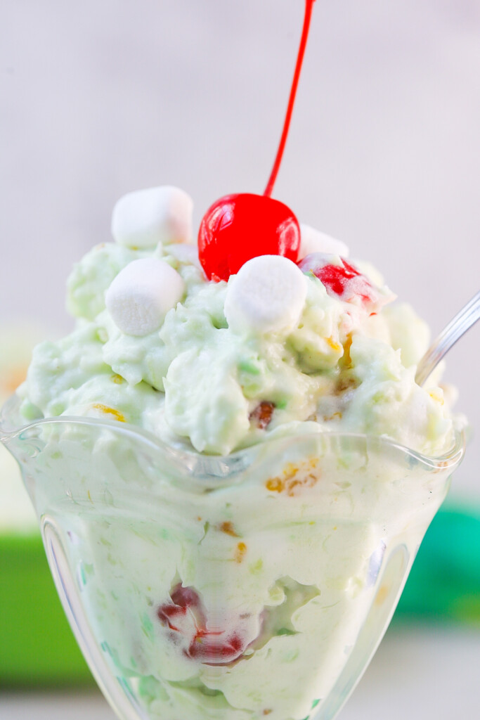 Close up with watergate salad in a sundae cup with mini marshmallows and a cherry on top