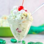 Ambrosia Watergate Salad with Coconut in a sundae glass topped with a cherry surrounded by green decorations