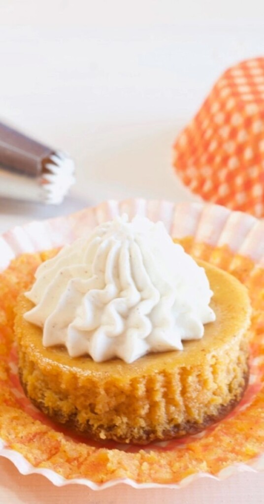 Easy mini pumpkin cheesecake topped with whipped cream with an orange cupcake wrapper