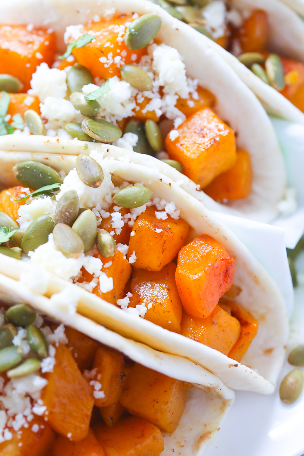 Four butternut squash tacos in flour tortillas topped with cojita cheese and green pepitas