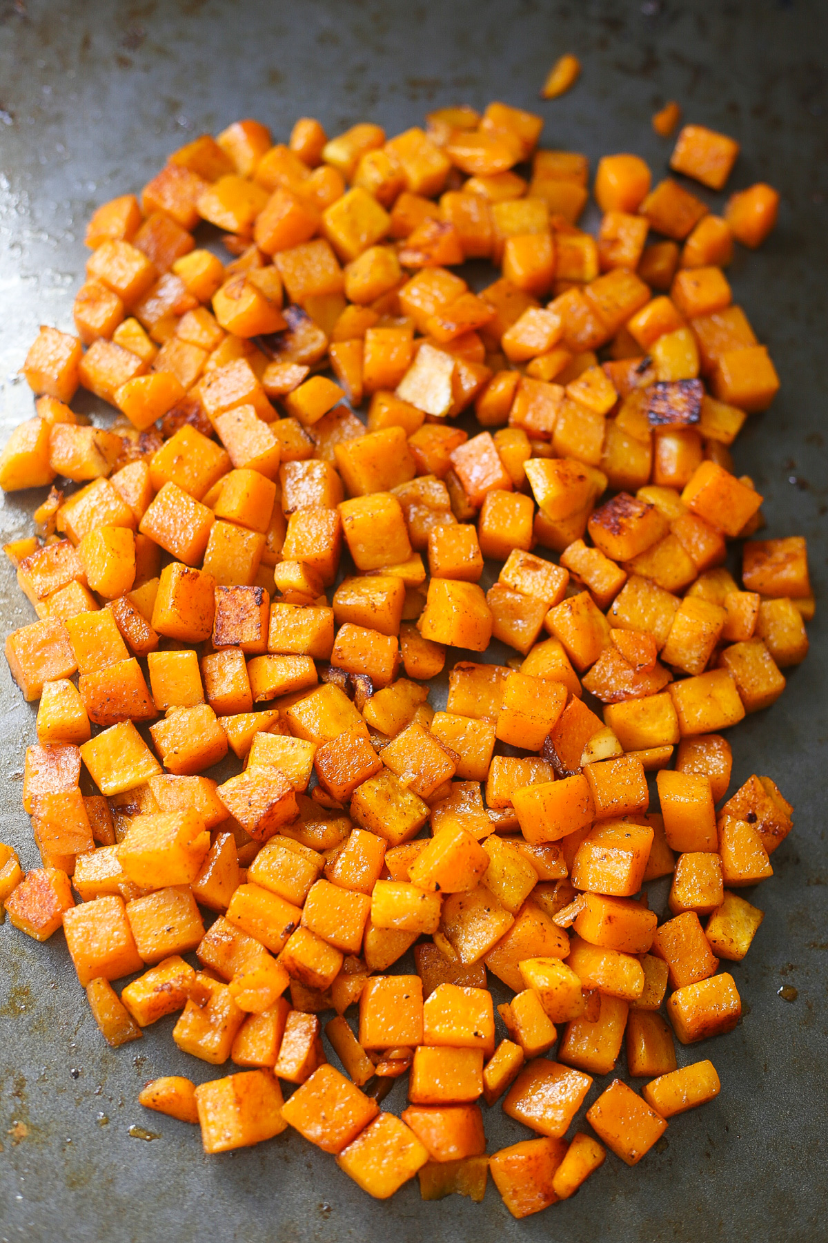 cubed and roasted honeynut butternut squash on a dark gunmetal baking sheet