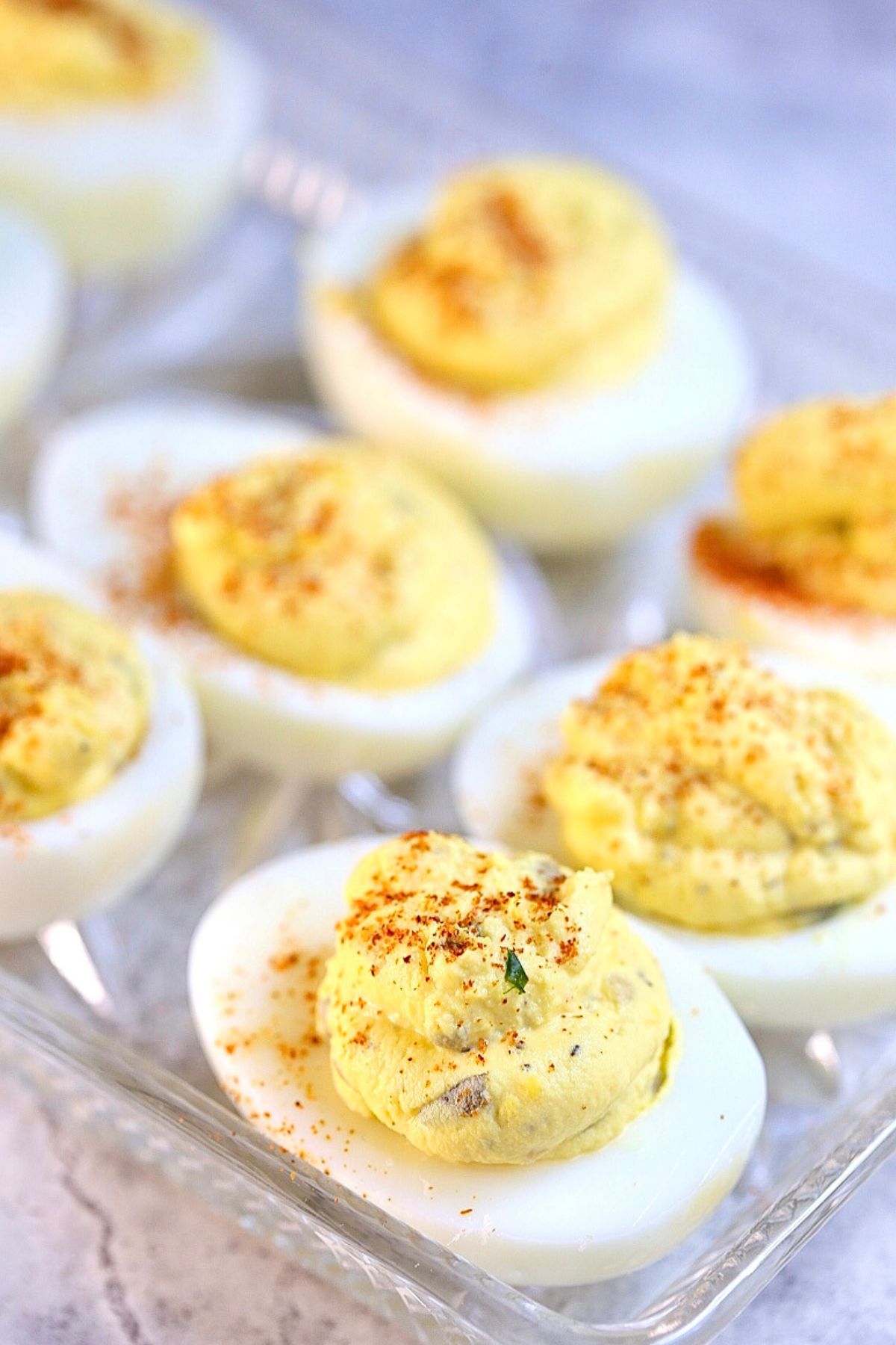 Prepared deviled eggs on a clear tray garnished with paprika, relish, and pickles