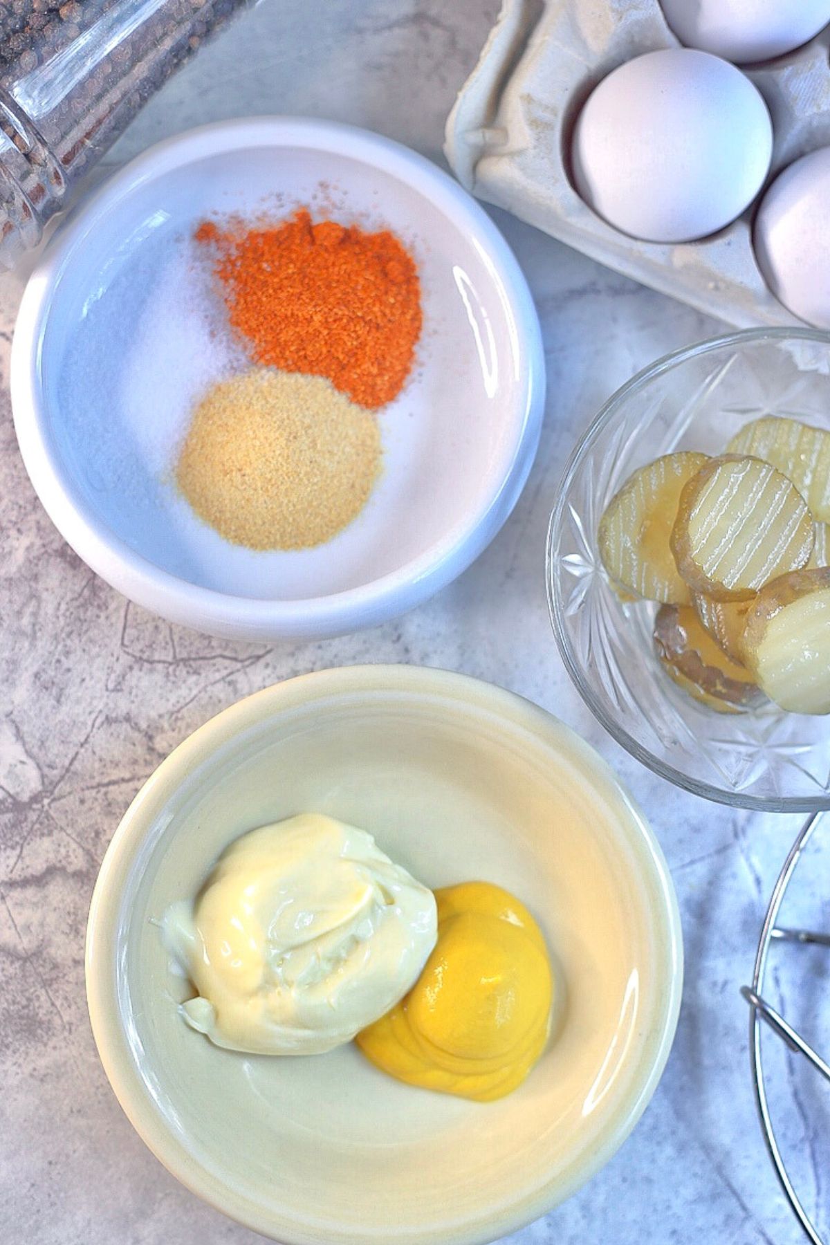 Overhead photo of southern deviled eggs with relish or pickles ingredients (mayo, mustard, garlic powder, salt, paprika, relish or pickles) on white plates on a table 